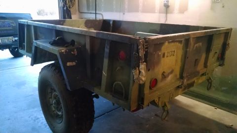 1979 Ford Bronco - A camouflaged military-style trailer is parked in a garage, with a portion of a dark pickup truck visible to the left. The trailer has larg…