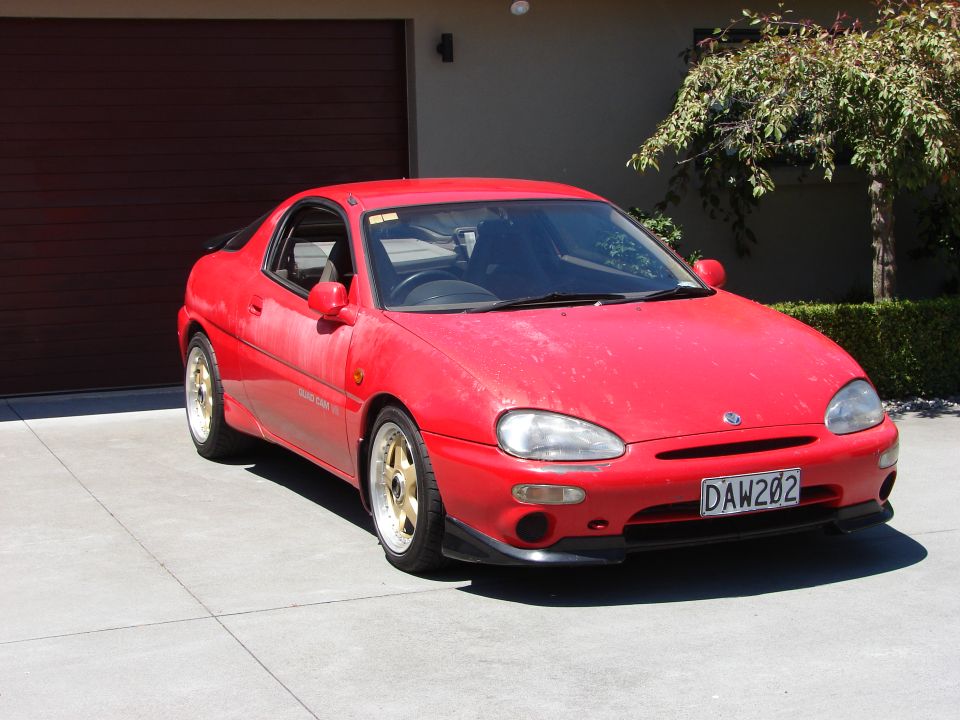 Red 1993 Mazda MX-3 (AKA Eunos Presso) with gold rims parked in front of a garage.