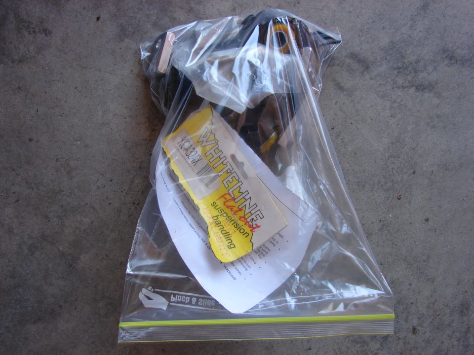 Plastic bag with Whiteline suspension parts and instructions on concrete.