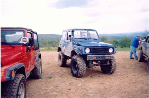 1978 Ford Bronco - Two off-road vehicles, a blue Suzuki Samurai and a red Jeep Wrangler, are parked on a dirt path with a man leaning on another vehicle in th…