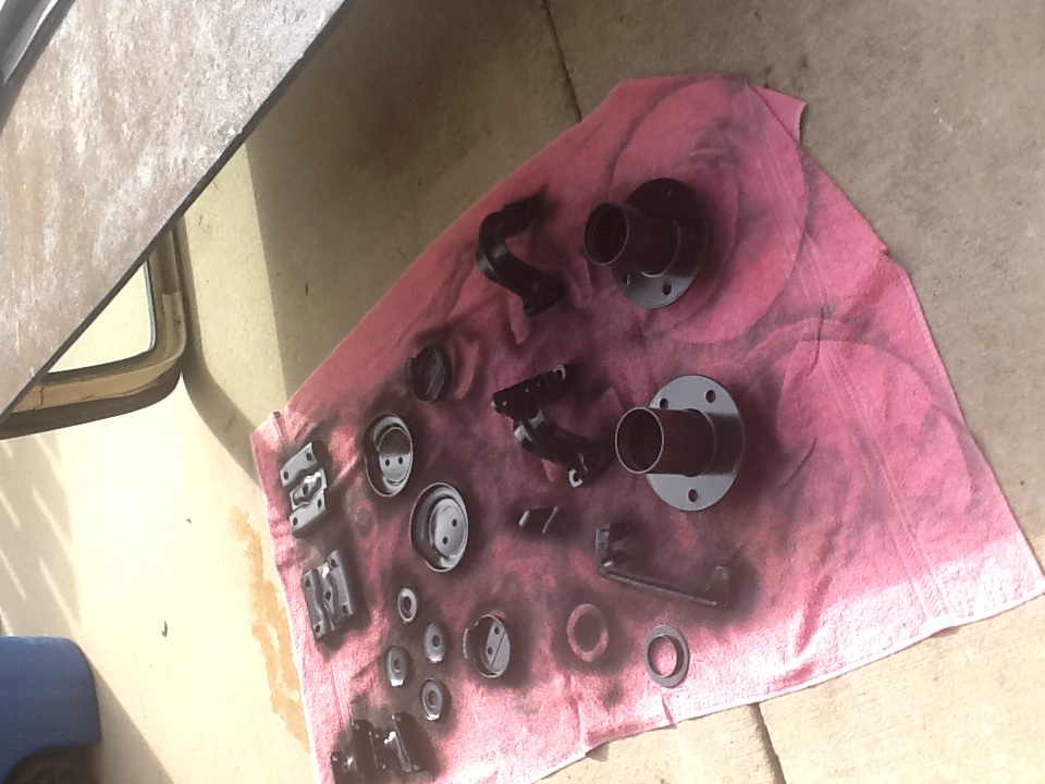 Various black automotive parts laid out on a pink cloth on concrete. Some parts have spray paint overspray
