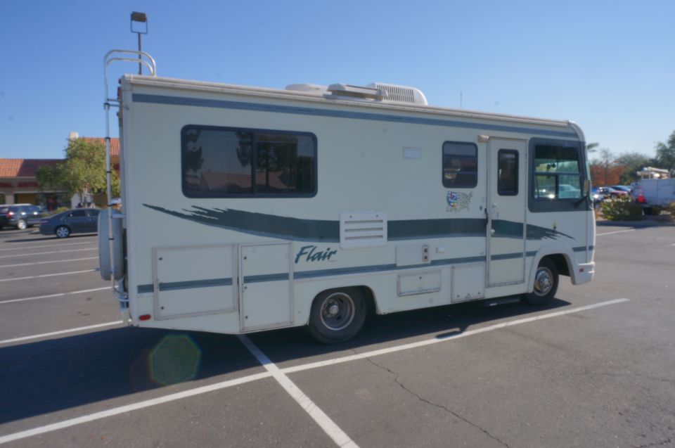 RV parked in a lot, side view. It has a ladder on the back and a 'Flair' decal