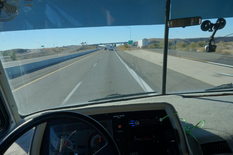View from driver's seat of a motorhome on highway, showing dashboard and steering wheel.