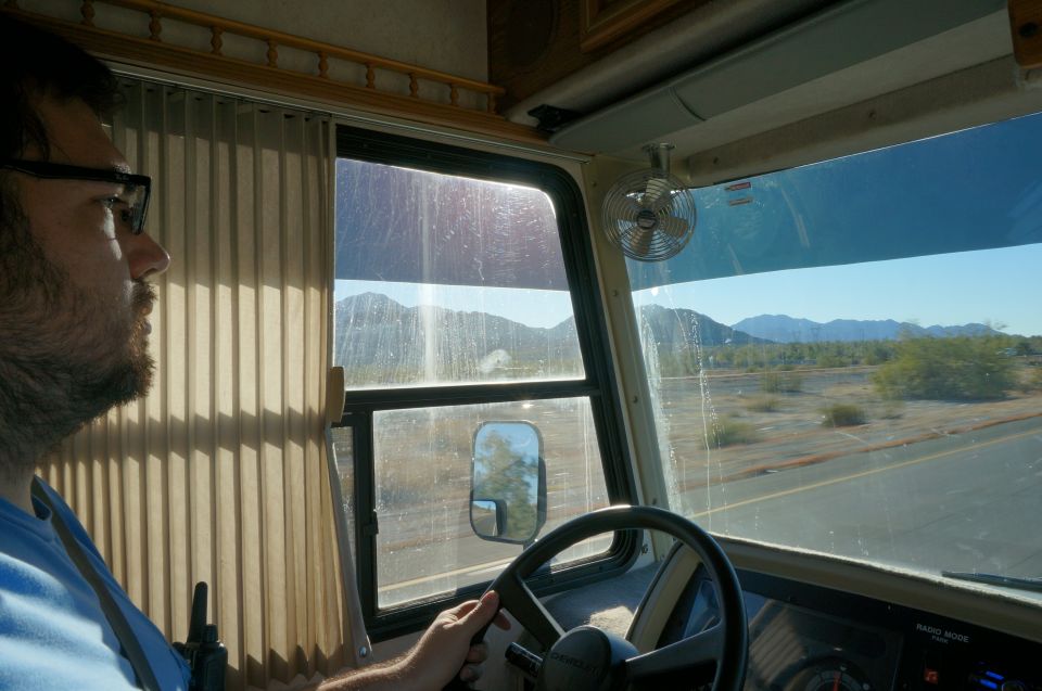 Man driving a motorhome through a desert landscape with mountains.
