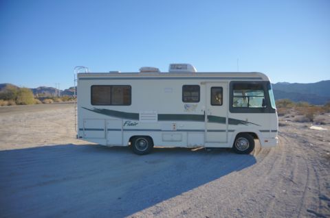 1995 Chevrolet P30 1 Ton - Step Van - A white and green Class A RV, labeled "Flair 22D" on the side, is parked on a dirt road in a desert landscape under a clear blue sky.