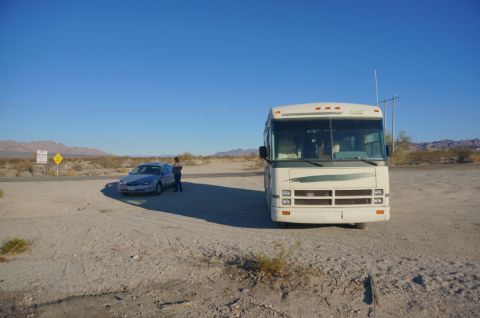 1995 Chevrolet P30 1 Ton - Step Van - White Class A motorhome and a silver sedan parked at a dirt-road junction in the desert with a person standing between them.