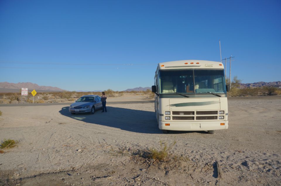 White Class A motorhome and silver sedan parked at a desert dirt junction