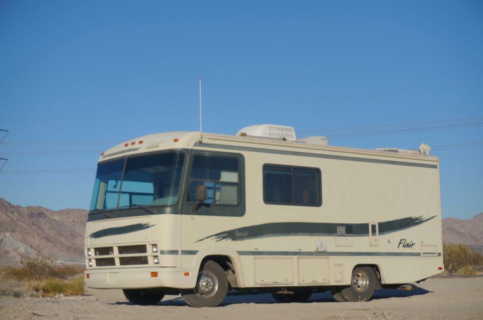Cream-colored RV with green graphics, parked in a desert landscape.