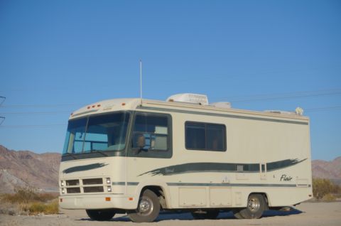 1995 Chevrolet P30 1 Ton - Step Van - A cream-colored RV with dark green pinstriping is parked on a dirt lot with mountains in the background. The RV has a large windshield, mul…