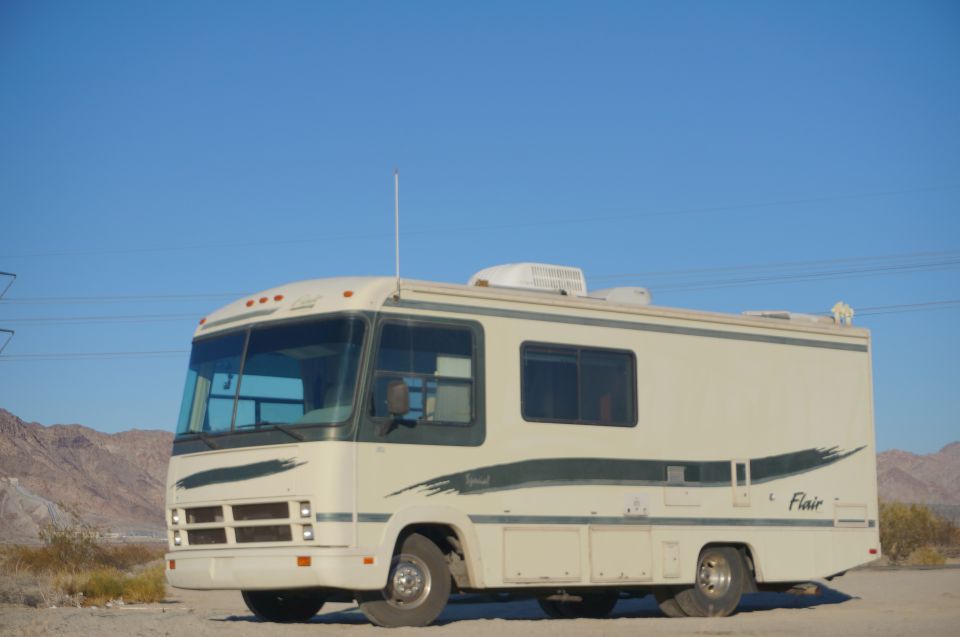 Cream-colored RV with dark green pinstriping parked on dirt lot.