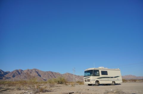 1995 Chevrolet P30 1 Ton - Step Van - A beige and green Class A RV is parked in a dry, desert landscape with mountains in the background under a clear blue sky.