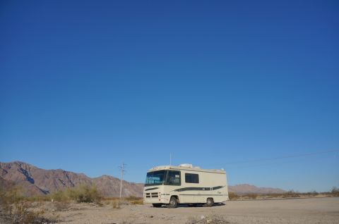1995 Chevrolet P30 1 Ton - Step Van - A white RV with green trim is parked in a desert landscape under a clear blue sky. Mountains are visible in the background.