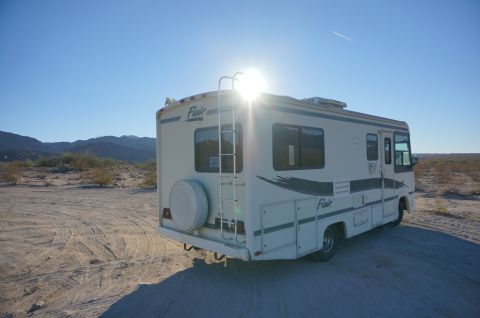 1995 Chevrolet P30 1 Ton - Step Van - A white Fleetwood Flair RV is parked in a dry, dusty, desert landscape under a clear blue sky. The sun is shining brightly behind the RV, c…