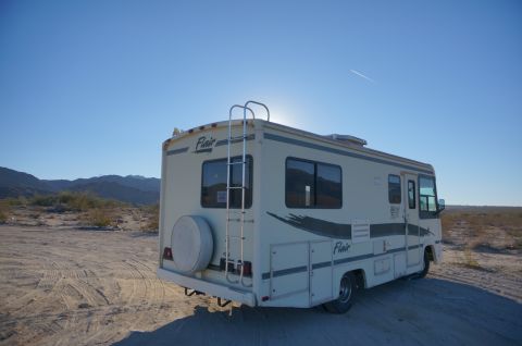1995 Chevrolet P30 1 Ton - Step Van - The rear and side of a white motorhome is parked on a dirt road in a desert landscape. A ladder is attached to the rear of the vehicle, and…