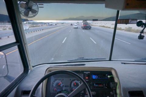 1995 Chevrolet P30 1 Ton - Step Van - View from the driver's seat of a step van driving on a highway through a desert landscape. The dashboard with gauges and a fan are visible.