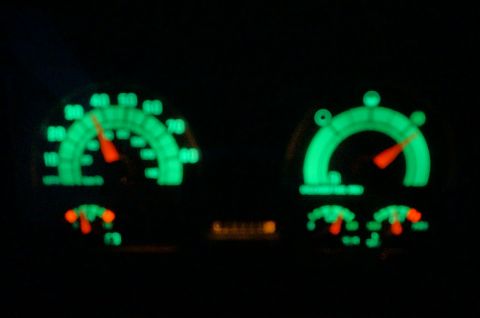 1995 Chevrolet P30 1 Ton - Step Van - The image shows a close-up of a vehicle's dashboard at night, featuring two glowing green gauges with orange needles. The gauge on the left…