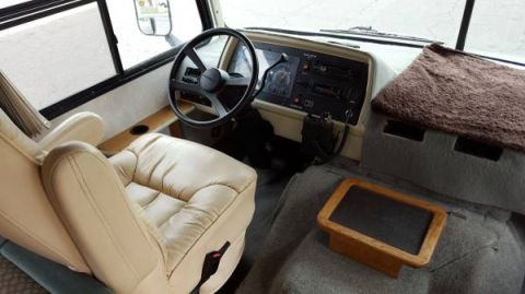 1995 Chevrolet P30 1 Ton - Step Van - The interior of a recreational vehicle shows the driver's seat, steering wheel, and dashboard. A small wooden tray with a dark insert sits…