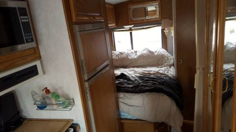 1995 Chevrolet P30 1 Ton - Step Van - The interior of a recreational vehicle shows a bed with a dark comforter, a small refrigerator, and a microwave oven above a control panel.