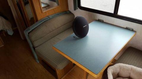1995 Chevrolet P30 1 Ton - Step Van - A black oval speaker sits on a teal table inside what appears to be an RV or camper van. A built-in bench seat with patterned upholstery is…
