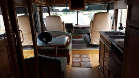 1995 Chevrolet P30 1 Ton - Step Van - Interior view of the driver and passenger seats of a recreational vehicle, with a small table and speaker visible in the foreground.