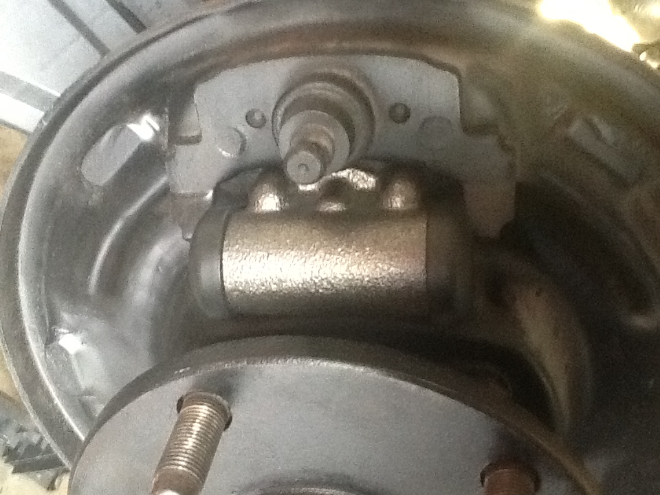 Close-up of internal drum brake components: wheel cylinder, brake shoes, and drum.