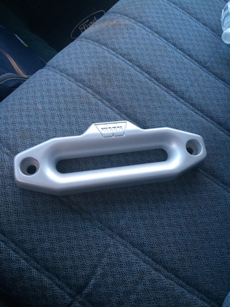 1981 Ford Bronco - A silver WARN hawse fairlead is shown resting on a textured gray seat, likely inside a vehicle. The fairlead has two mounting holes and the…