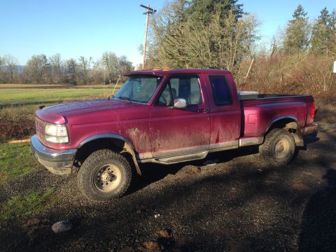 1992 Ford F-150 - A maroon 1992 Ford F-150 pickup truck is shown from the side, parked on a gravel surface with a field in the background.