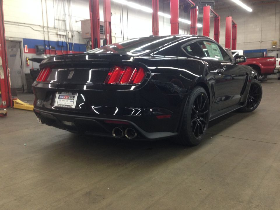 Black sports coupe in a garage, rear view. Has quad exhaust tips and a spoiler