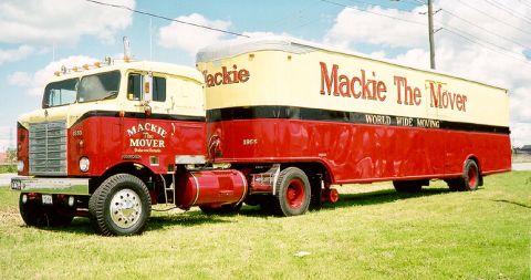 1995 Peterbilt 379 - A vintage Mackie The Mover semi-truck and trailer is parked on a grassy field under a cloudy sky.