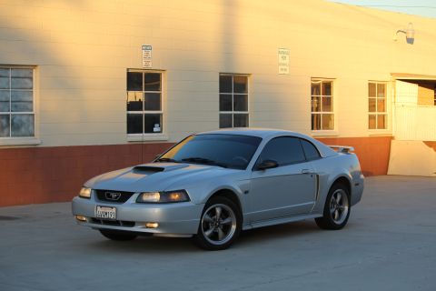 2002 Ford Mustang - A silver 2002 Ford Mustang coupe is parked in front of a building with windows.