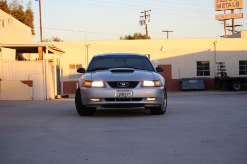 2002 Ford Mustang - A silver 2002 Ford Mustang is parked in front of a commercial building with a sign that says 'ABOUT METALS'.
