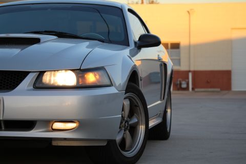 2002 Ford Mustang - The front end of a silver 2002 Ford Mustang is shown in a three-quarter view, with the headlights on.