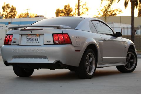 2002 Ford Mustang - The rear passenger side of a silver 2002 Ford Mustang GT is shown at a low angle with the sun setting behind it. The car has a California l…