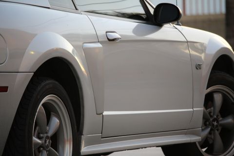 2002 Ford Mustang - Close-up side view of a silver Ford Mustang GT's front fender, door, and wheel. The vehicle features a GT badge on the fender and a five-sp…