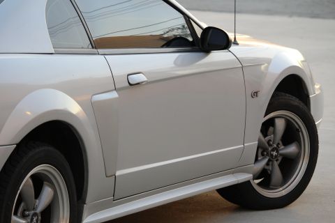 2002 Ford Mustang - Close-up side view of a silver Ford Mustang GT showing the driver's side door, fender, and wheel. The car features a GT badge on the front…