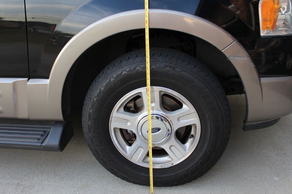 Yellow measuring tape against the fender and tire of a black and tan SUV.