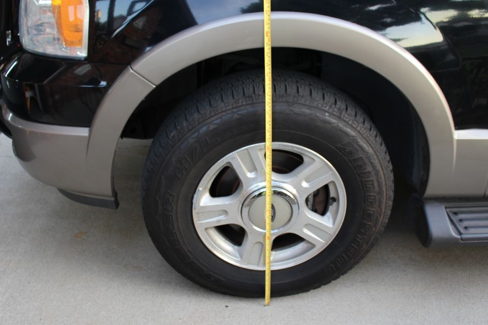 Yellow measuring tape next to front tire of a black SUV, showing fender clearance.