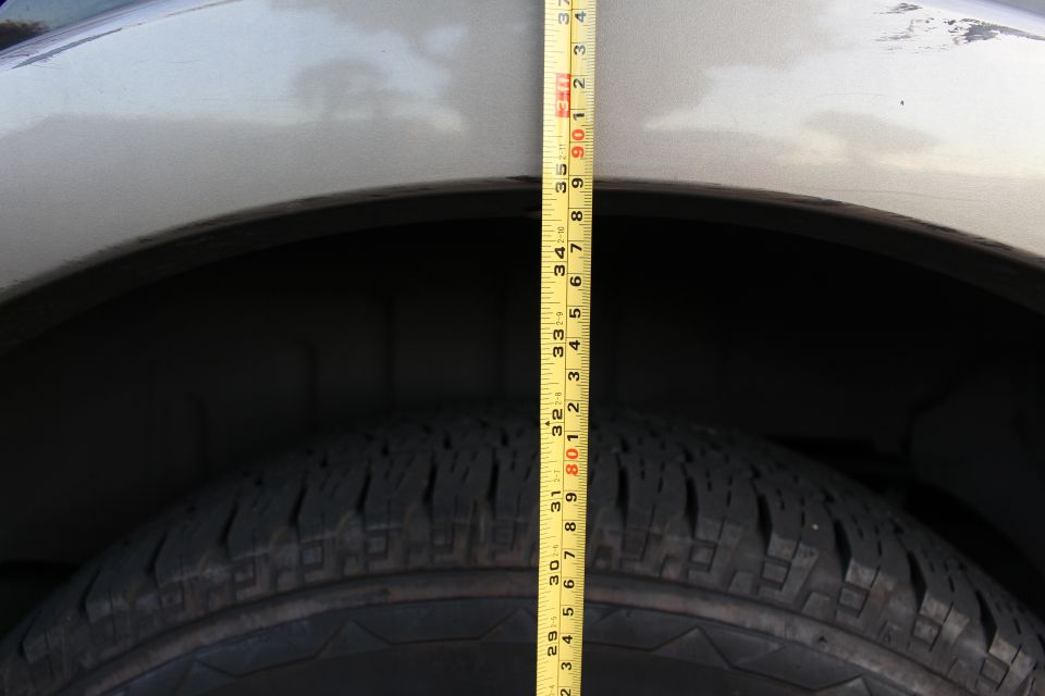 Measuring the distance from tire to fender on a light-colored SUV.