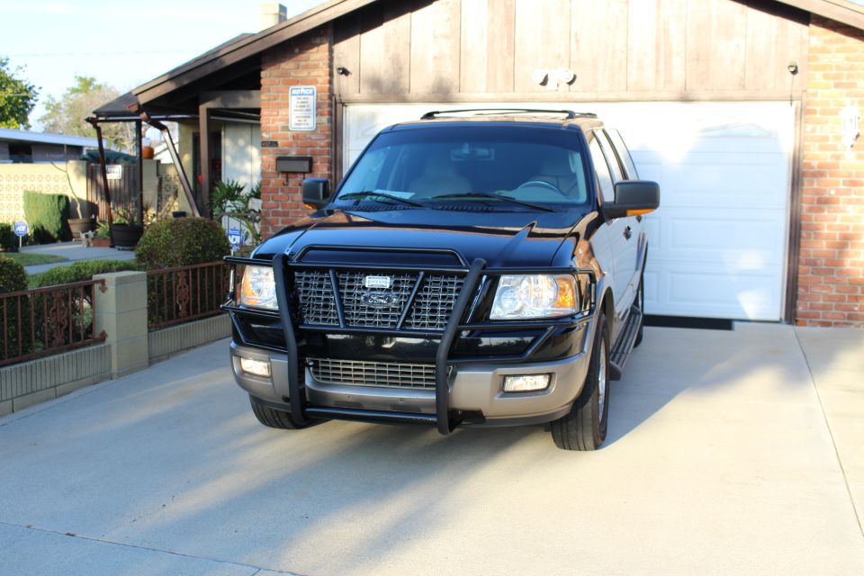Black Ford Expedition with brush guard parked in front of a garage.