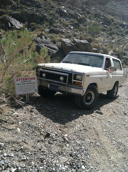 1981 Ford Bronco - A white 1980s Ford Bronco is parked on a gravel road next to a sign that reads "ATTENTION CLOSED TO FULL SIZE VEHICLES". The vehicle is in…