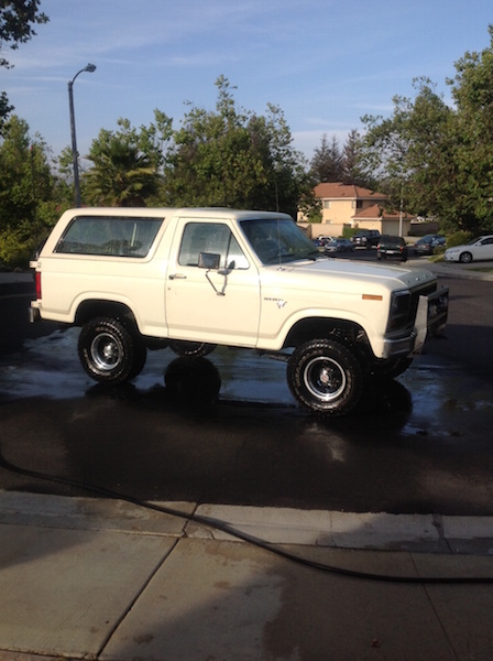 1981 Ford Bronco - A white 1980s Ford Bronco is parked on a wet asphalt surface, likely after being washed. The vehicle is viewed from the side, showcasing it…