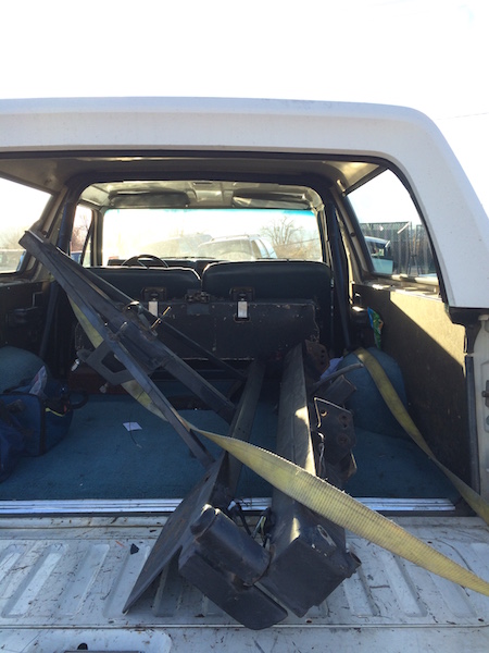 1981 Ford Bronco - The rear cargo area of a white SUV, likely a 1981 Ford Bronco, is filled with various black metal parts and a yellow strap. The interior fe…
