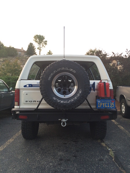 1981 Ford Bronco - The rear view of a white Ford Bronco is shown, featuring a spare tire mounted on the back, a red jerry can, and a California license plate.…