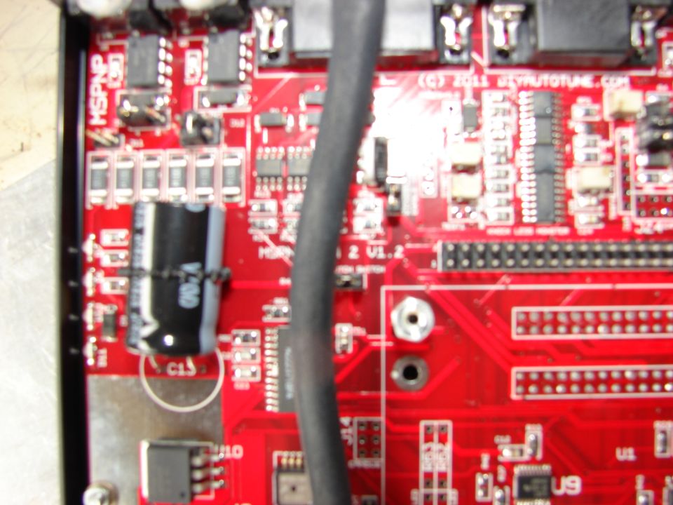 Close-up of a red circuit board with electronic components and a black cable.