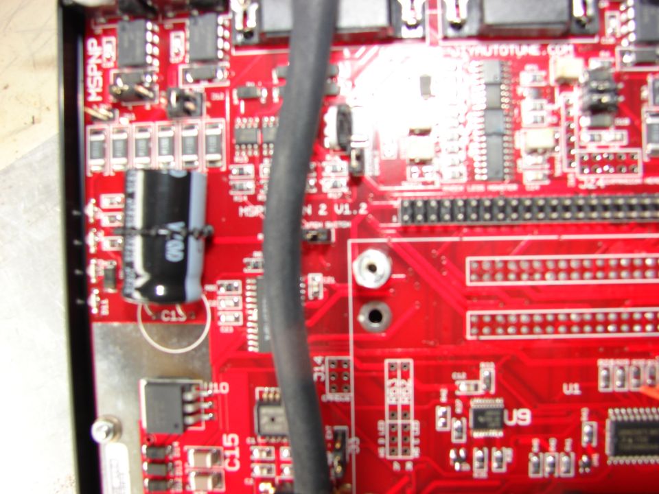 Close-up of a red circuit board with electronic components and a black cable.