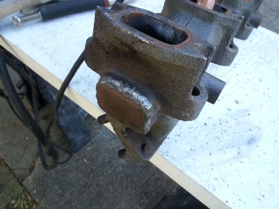 Welded metal exhaust manifold part on a workbench.