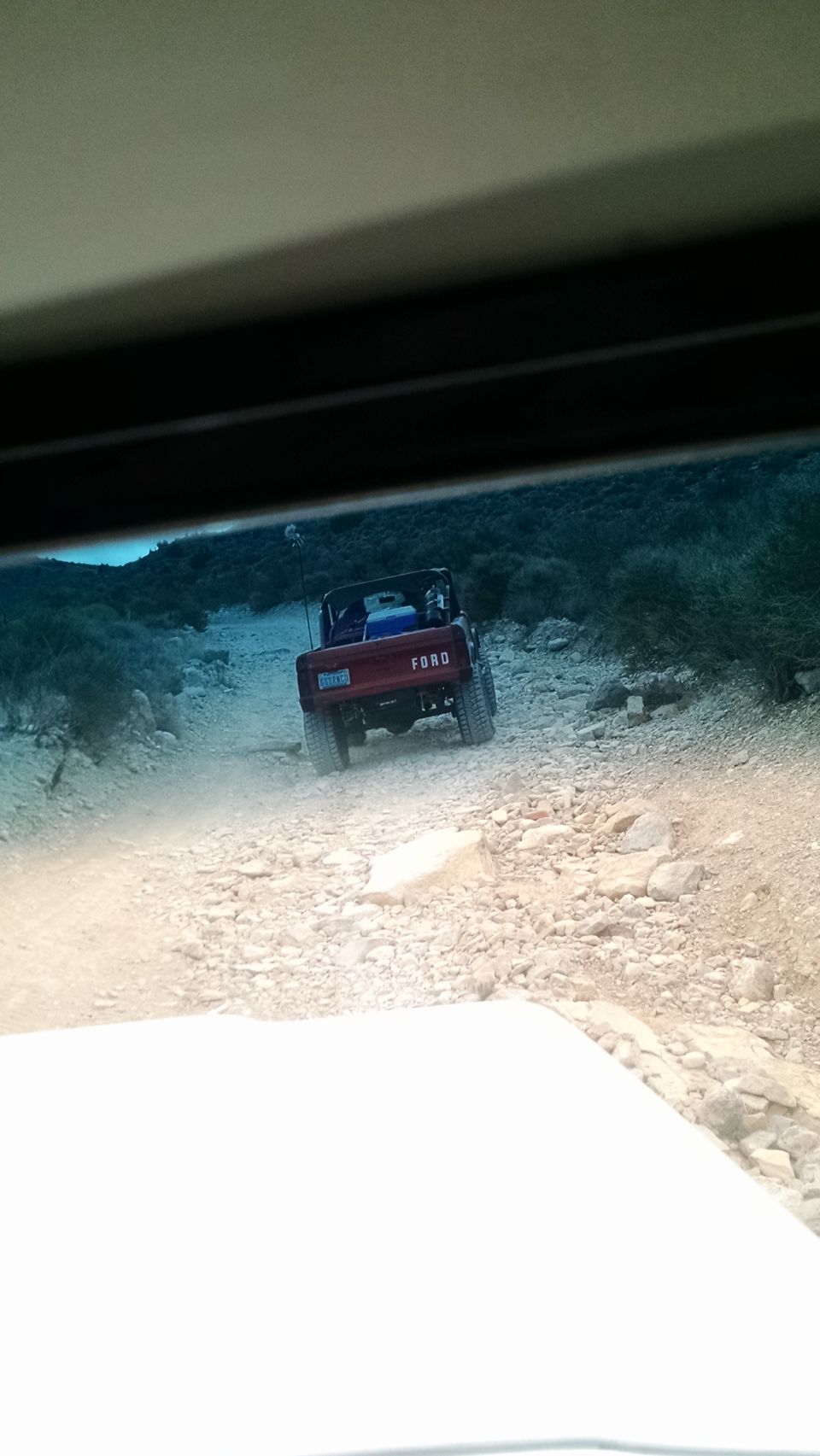 Red 1979 Ford Bronco driving on a rocky off-road trail, viewed from the rear.