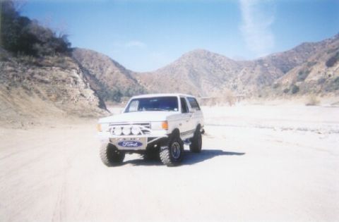 1988 Ford Bronco - A white Ford Bronco is parked in a dry, dusty landscape with mountains in the background.