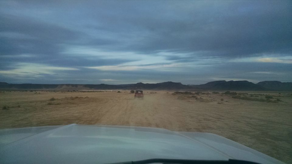 View from a white vehicle's hood looking at a red off-road vehicle in a dusty desert.