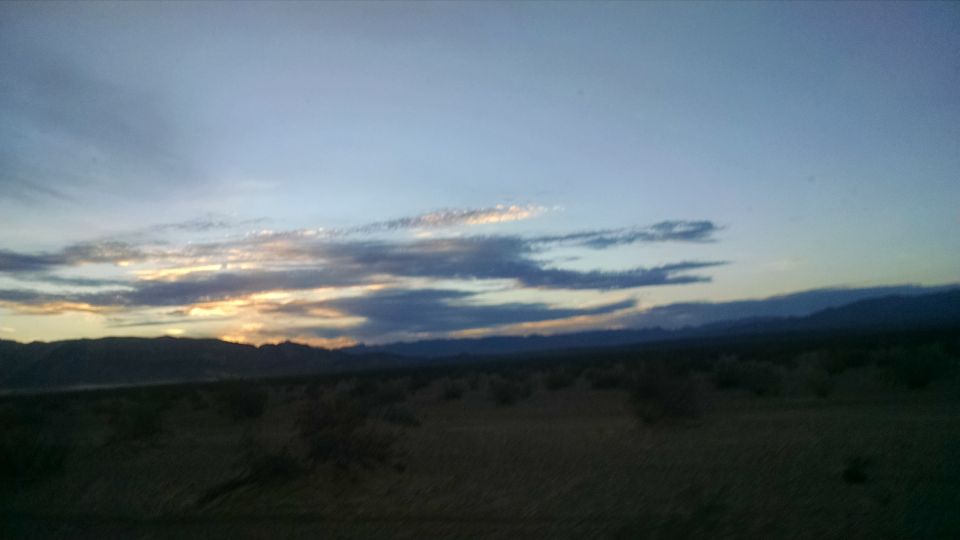 Desert landscape at dusk with silhouetted mountains and wispy clouds.